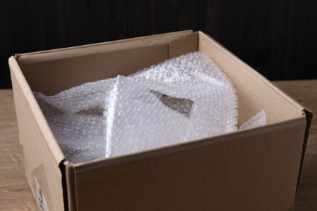 Bubble wrap in cardboard box on wooden table, closeup