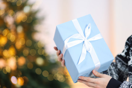 Person with Christmas gift against blurred lights, closeup. Space for text