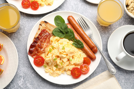 Tasty breakfast. Delicious scrambled eggs with bacon, sausages and tomatoes served on gray textured...