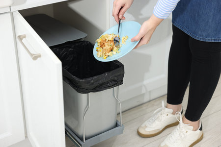 Woman throwing food waste into trash bin in kitchen, closeupの写真素材