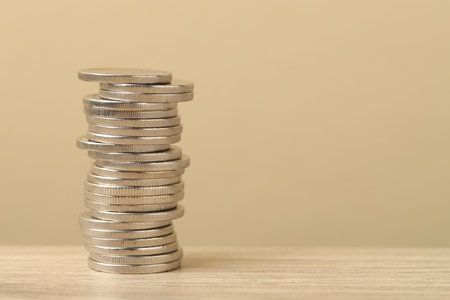Stack of coins on wooden table against beige background, closeup. Space for text