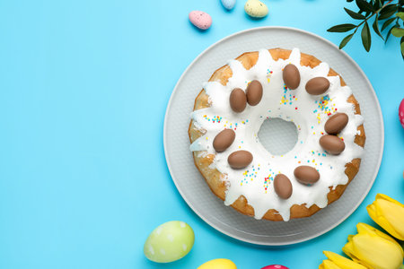 Delicious Easter cake, painted eggs, beautiful tulips and green leaves on light blue background,...