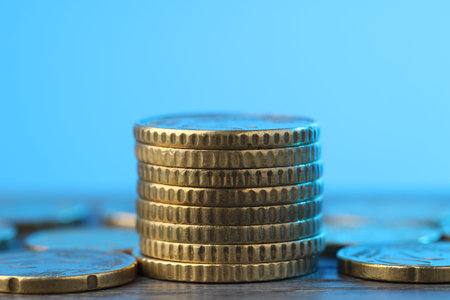 Stack of coins on wooden table against light blue background, closeup