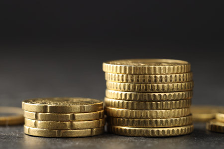 Many stacked coins on table against blurred background, closeup
