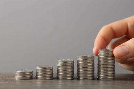 Woman stacking coins at wooden table against gray background, closeup