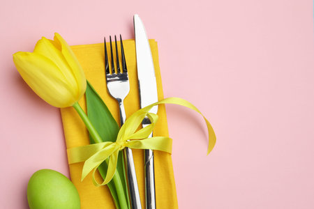 Easter celebration. Festive table setting with floral decor and painted egg on pink background, flat...
