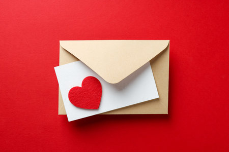 Happy Valentine's day. Envelope with greeting card and decorative heart on red background, top view