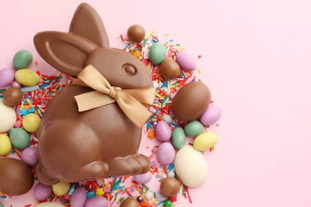 Chocolate Easter bunny, eggs, candies and sprinkles on pink background, flat lay. Space for text