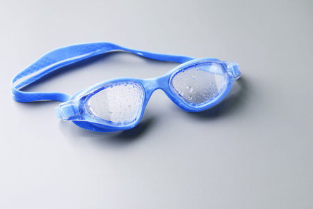 Swimming goggles with water drops on gray background, closeup