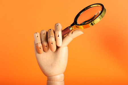 Mannequin hand with magnifying glass on orange background, closeupの写真素材