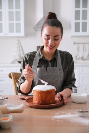 Young woman decorating traditional Easter cake with glaze in kitchen