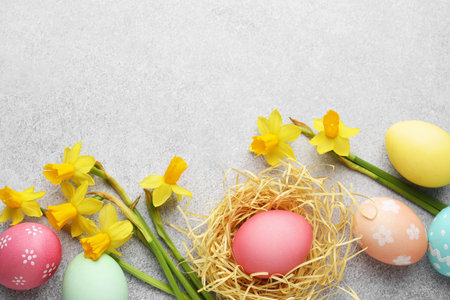 Painted Easter eggs in nest and beautiful daffodils on gray textured table, flat lay. Space for text
