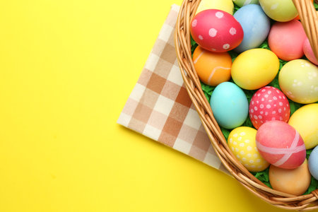 Easter basket with painted eggs on yellow background, top view. Space for text