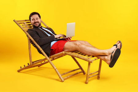 Office worker with laptop in deck chair on orange backgroundの写真素材