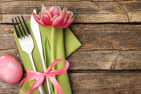 Easter table setting. Beautiful silverware with tulip and painted egg on wooden background, top...