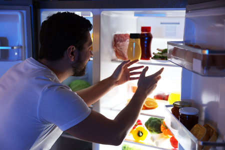Man looking into open refrigerator in kitchenの写真素材