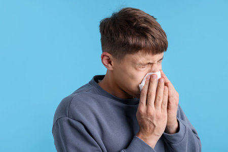 Young man with runny nose on light blue background, space for text. Cold symptomの写真素材