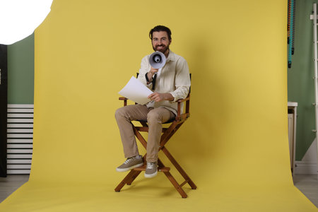 Professional film director with megaphone and script on chair against yellow backgroundの写真素材