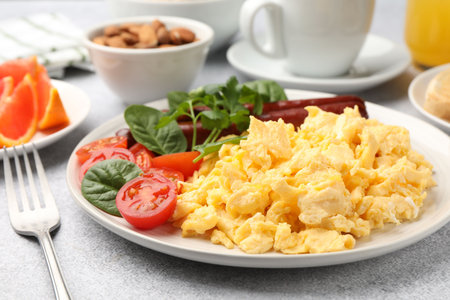 Tasty breakfast. Delicious scrambled eggs with sausages and tomatoes on gray textured table, closeup