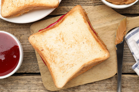 Tasty peanut butter sandwich with jam on wooden table, flat lay
