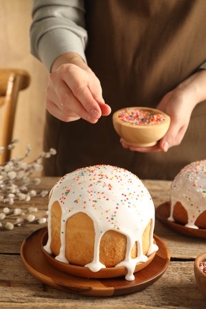 Woman putting sprinkles on Easter cake at wooden table, closeup