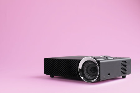 Modern video projector on pink background, space for text