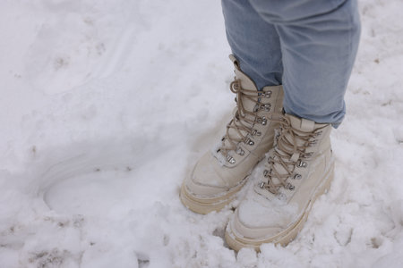 Woman in stylish winter shoes standing on snow outdoors, closeup. Space for text