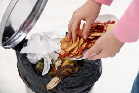 Woman throwing apple peels into garbage can in kitchen, closeup