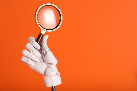 Mannequin hand with magnifying glass on orange background, closeup. Space for textの写真素材