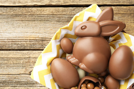Chocolate Easter bunny and eggs in bowl on wooden table, top view. Space for text