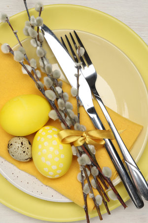 Festive table setting with Easter eggs and willow branches on white wooden background, top view