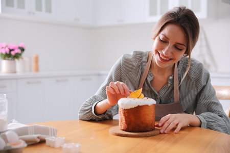 Young woman decorating traditional Easter cake in kitchen. Space for text