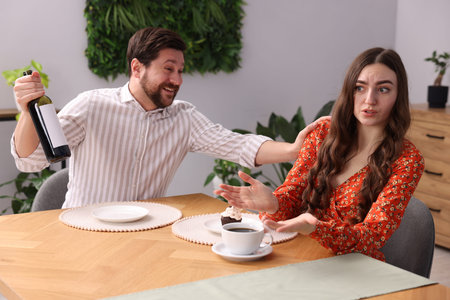 Bad date. Embarrassed woman and man with bottle of wine at table during dinner indoors
