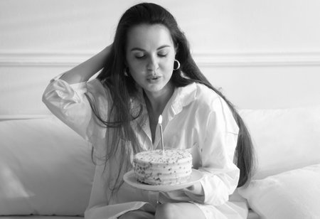 Birthday celebration. Woman with delicious cake on bed at home. Black and white effect