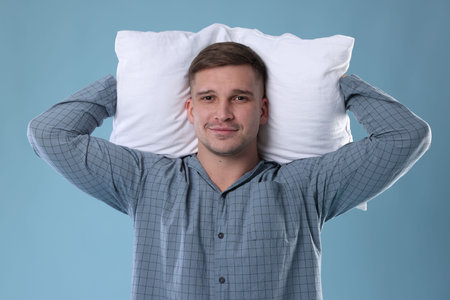 Man in stylish pajamas with pillow on light blue background