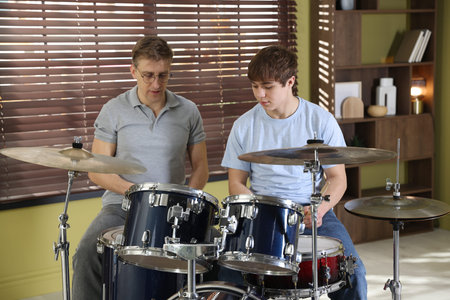 Teenage boy learning how to play drums with music teacher indoors