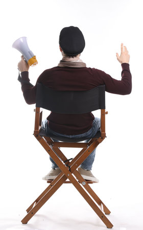 Professional film director with megaphone on chair against white background, back view