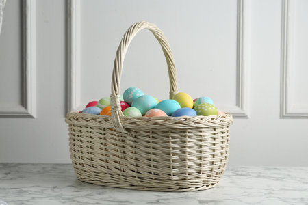 Painted Easter eggs in wicker basket on white marble table near white wall