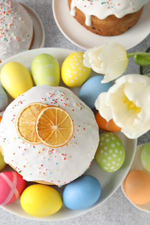 Tasty Easter cakes, tulips and painted eggs on light grey table, flat lay