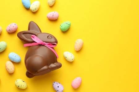 Chocolate Easter bunny and eggs on yellow background, flat lay. Space for text