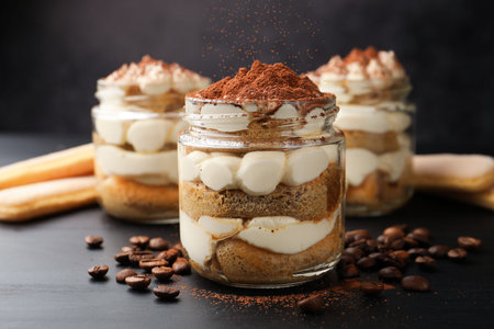 Delicious tiramisu in jars, coffee beans and savoiardi biscuit cookies on dark wooden table, closeupの写真素材