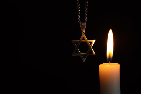 Holocaust Remembrance Day. Pendant in shape of Star of David and burning candle against black background, closeup. Space for textの写真素材