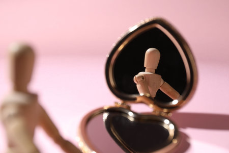 Wooden mannequin with pocket mirror on pink background, closeup