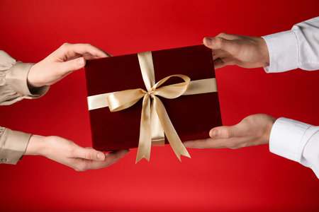 Valentine's Day. Woman giving gift to her boyfriend on red background, closeup