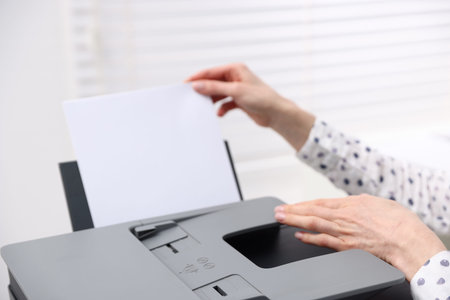 Woman loading paper into printer near window indoors, closeup