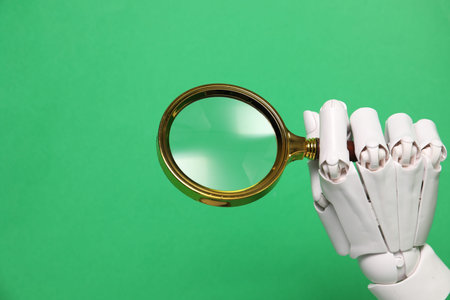 Mannequin hand with magnifying glass on green background, closeup. Space for text