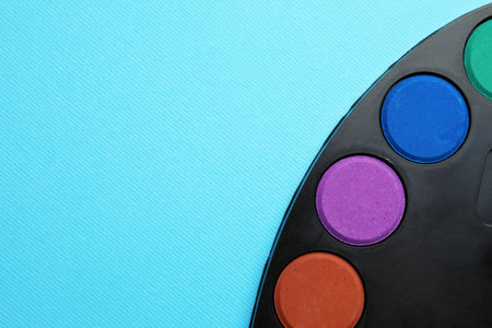 Watercolor palette on light blue background, top view. Space for text