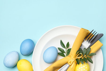 Easter celebration. Festive table setting with green leaves and painted eggs on light blue...
