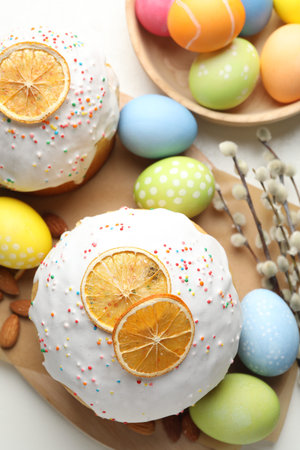 Tasty Easter cakes, painted eggs and willow branches on white table, flat lay