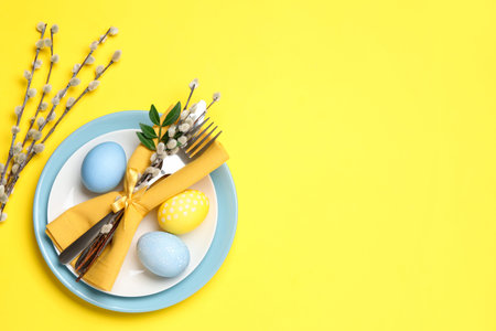 Easter celebration. Festive table setting with willow branches and painted eggs on yellow...